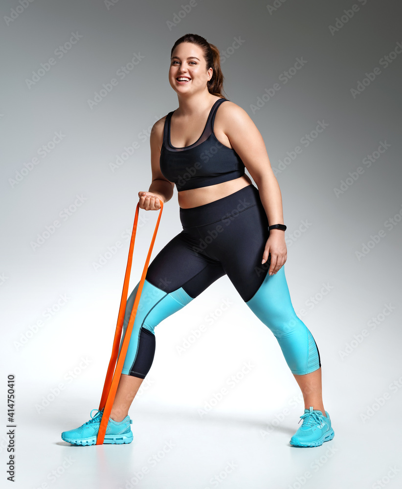 Sporty girl resting after workout with resistance band. Photo of model with curvy figure in fashionable sportswear on grey background. Sports motivation and healthy lifestyle Sporty girl resting after workout with resistance band. Photo of model with curvy figure in fashionable sportswear on grey background. Sports motivation and healthy lifestyle