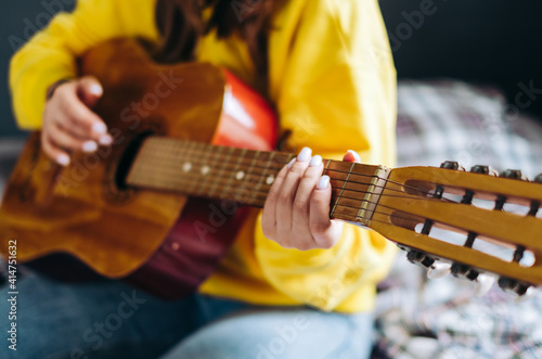 Closeup young woman's hand playing acoustic guitar at home.