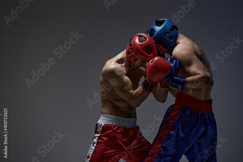 Foto Sparring of two fighting males in helmets and boxing gloves on gray studio backg