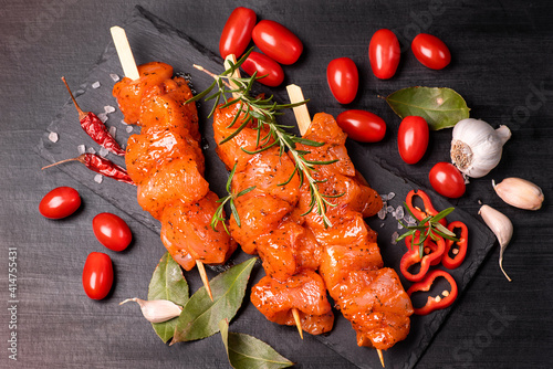 Chicken pieces of kebabs marinated in a red marinade with spices on a dark culinary board, on a background with pieces of pepper. Raw chicken pieces on skewers. Marinated chicken meat.
