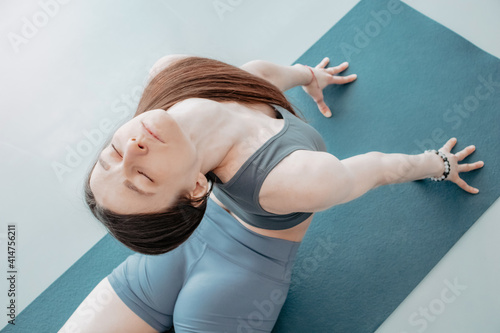 A young woman practices yoga on a mat in a gray tracksuit. Cobra pose. View from above.