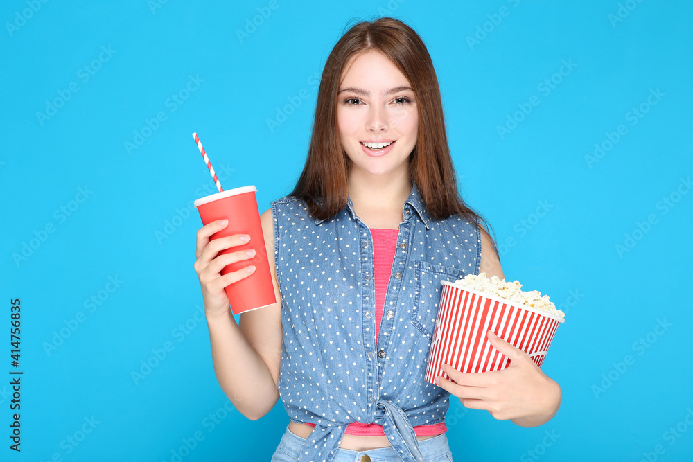 Beautiful girl with bucket of popcorn and drink on blue background Beautiful girl with bucket of popcorn and drink on blue background