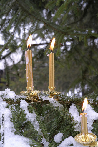 Clip-on candlesticks with burning candles on spruce branches covered with snow