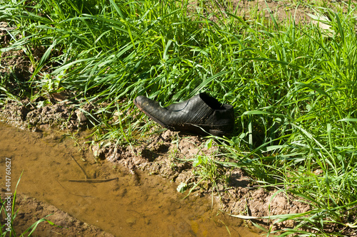Black shoe among green grass and mud