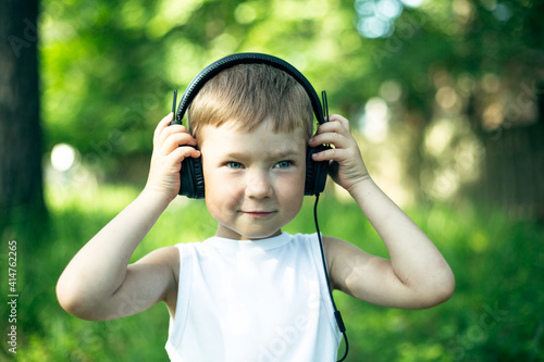 Portrait of little boy enjoying music in headphones, in the Park.