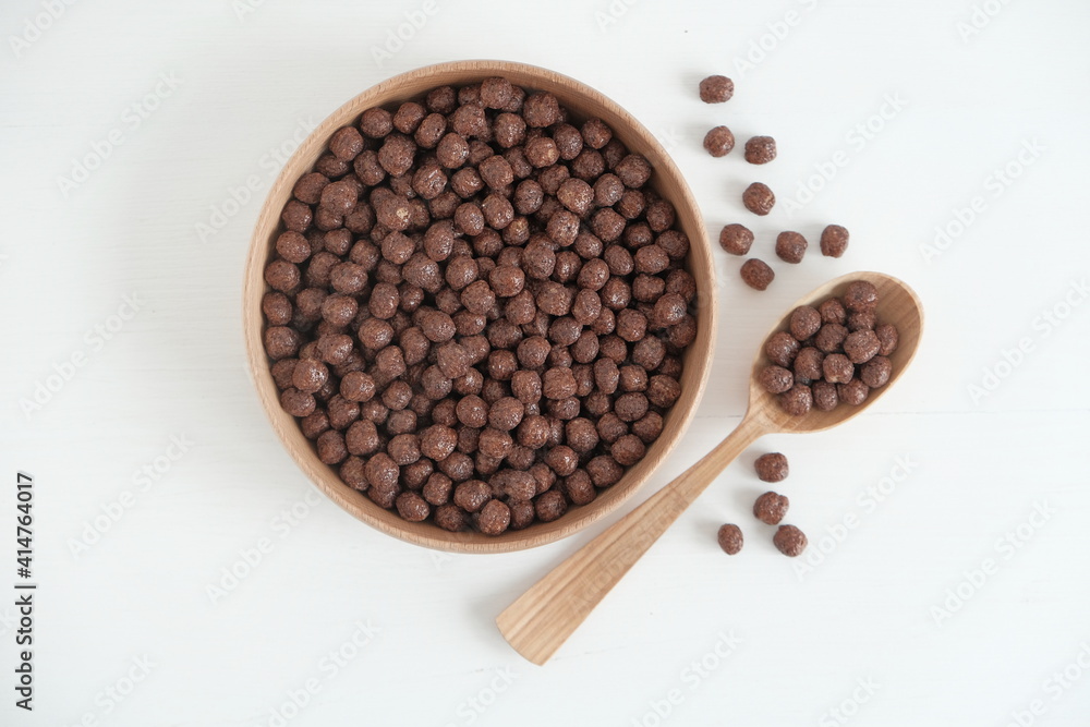 Fototapeta premium Chocolate corn balls in a wooden bowl and spoon scattered on a white background. Top view. Copy, empty space for text