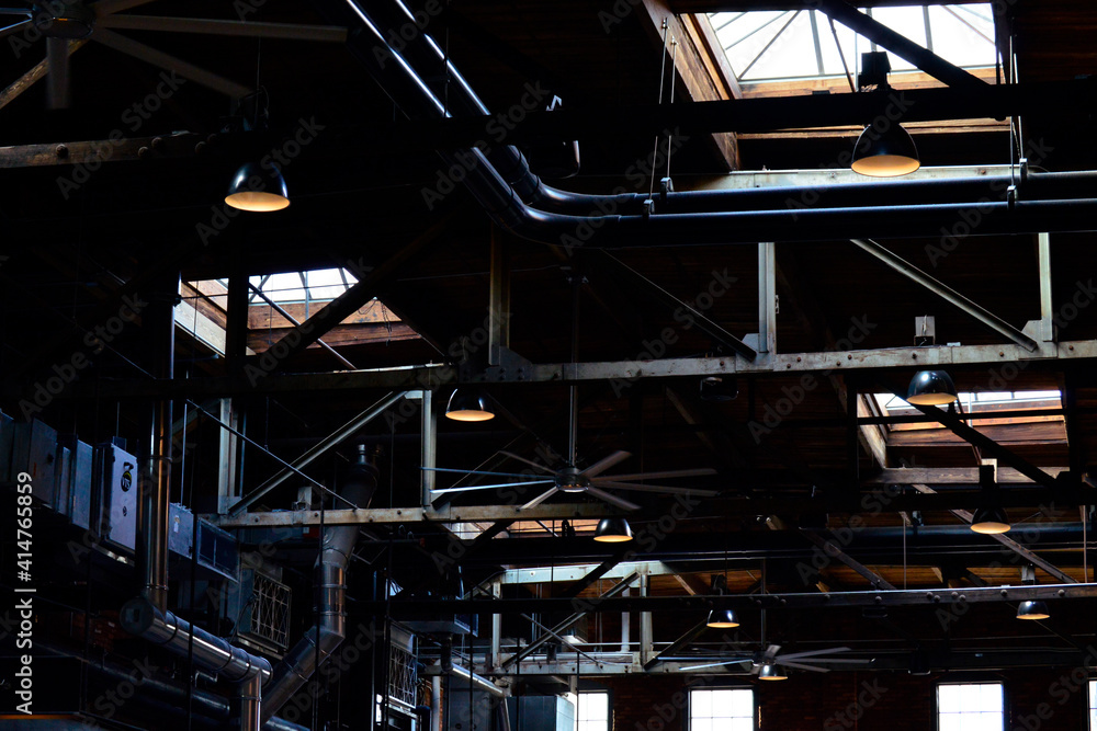 Pipes, ceiling fans, vents, and windows in a dark warehouse