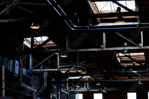 Pipes, ceiling fans, vents, and windows in a dark warehouse
