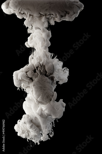 Ink dropped into the water and photographed while in motion. Paint swirling in water. Grey and white cloud and smoke of paint in water isolated on black background.