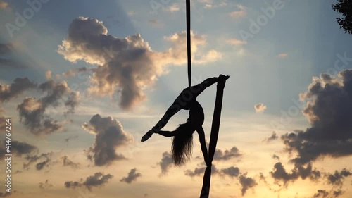 Female circus artist showing her flexibility and splits with red aerial silk on the sky background. Concept of healthy lifestyle