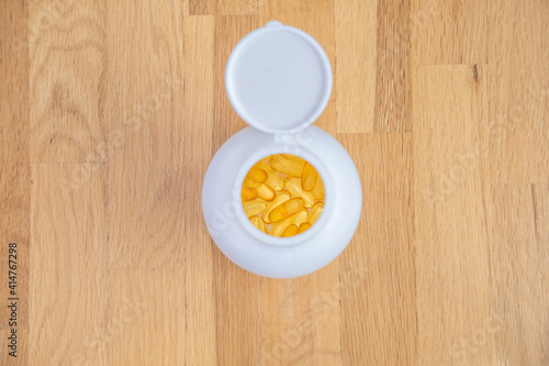 White jar with yellow transparent capsules of fish oil (omega-3, vitamin E) stands on a wooden table top view. Supplements and vitamins for sports and health in daily life