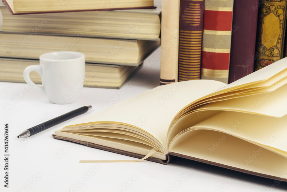 Fototapeta premium Open notebook with stack of books in background. Selective focus.