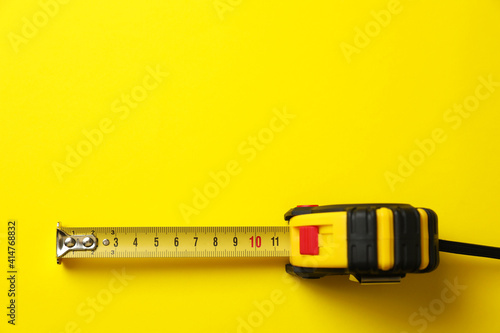 Tape measure on yellow background, top view. Space for text