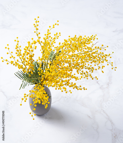 a bouquet of yellow mimosa flowers stands in a ceramic  vase on a marble background. concept of 8 March, happy women's day