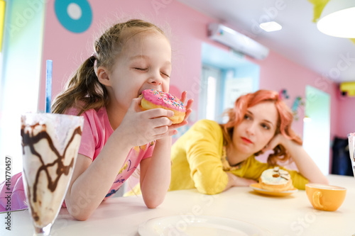 Little girl with mom eating a donut in a cafe