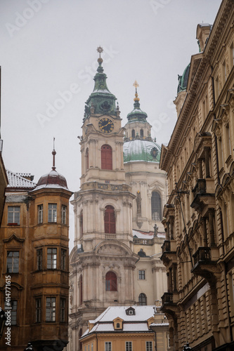 Mostecka Street with a view of the Church of Saint Nicholas, old town with historical buildings, snow in winter day, Mala Strana or Lesser Town district, Prague, Czech Republic © AnnaRudnitskaya