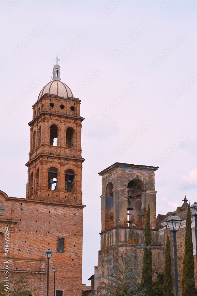 Contraste entre torres de iglesia antigua y nueva con cielo nublado