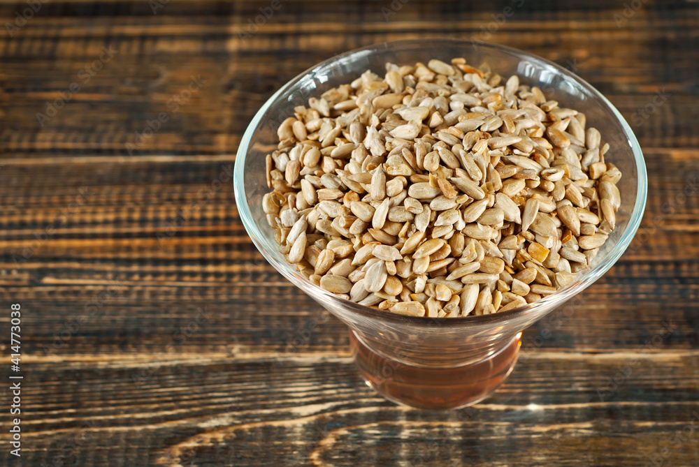 Sunflower seeds in a transparent glass bowl on an old shabby board. Nuts on a brown wooden table. Sunflower seeds in a transparent glass bowl on an old shabby board. Nuts on a brown wooden table.