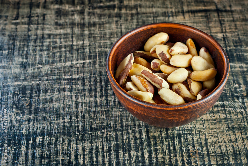 Brazil nuts in a clay bowl on a wooden table. Nuts on a black shabby board. Copy space and free space for text near nuts. Brazil nuts in a clay bowl on a wooden table. Nuts on a black shabby board. Copy space and free space for text near nuts.