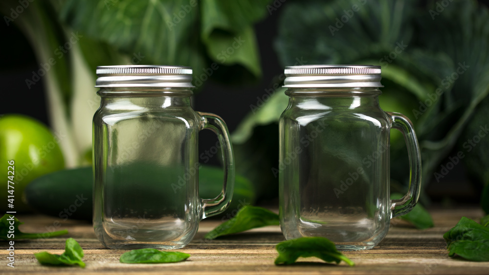 Glass jar. Mason Jar for drinking. Empty glass jar with lid and handle good for smoothie. Green Vegetables and fruits Ingredients on wooden table. Glass jar. Mason Jar for drinking. Empty glass jar with lid and handle good for smoothie. Green Vegetables and fruits Ingredients on wooden table.