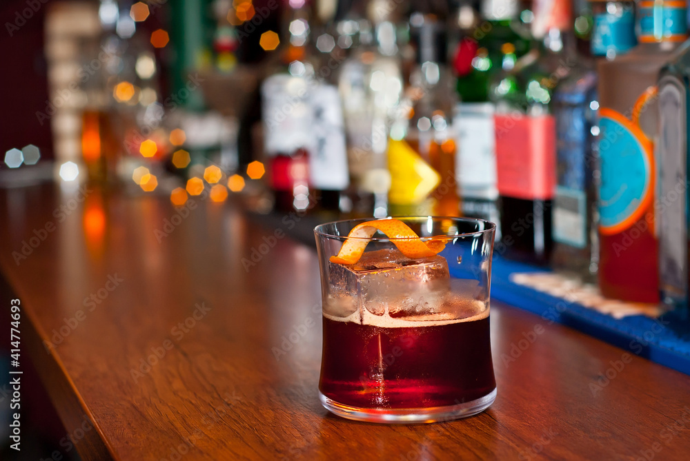 Yellow cocktail on bar counter. Whiskey, rum or brandy on the background of bottles with alcohol. Glass with booze on a wooden board. Yellow cocktail on bar counter. Whiskey, rum or brandy on the background of bottles with alcohol. Glass with booze on a wooden board.