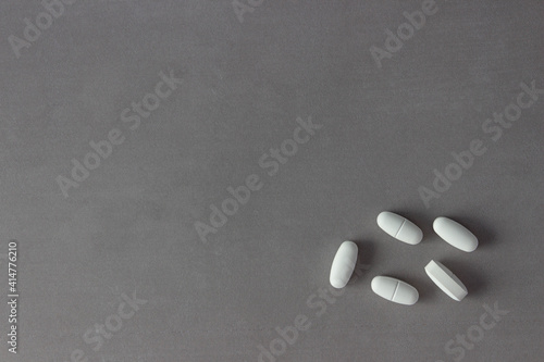 A handful of white pills in the bottom right corner of the photo on a stylish gray background. Minimalism. Background, banner. With copy space. Concept of medicine, treatment