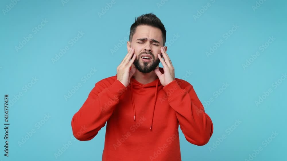 Sick ill young man 20s years old in red streetwear hoodie isolated on pastel blue background studio. People lifestyle concept. Put hands on head rub temples having headache migraine feel bad seedy Sick ill young man 20s years old in red streetwear hoodie isolated on pastel blue background studio. People lifestyle concept. Put hands on head rub temples having headache migraine feel bad seedy