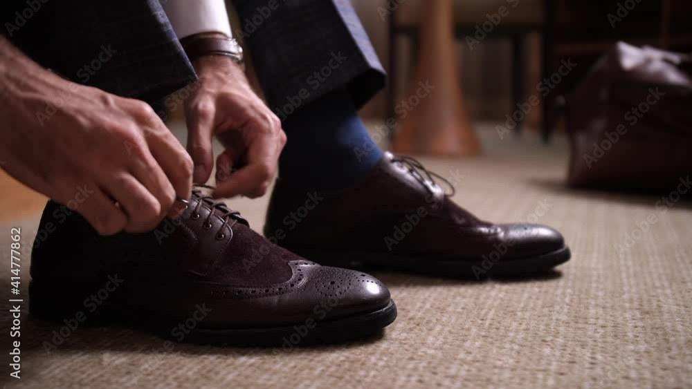 Close-up of male hands tying shoes, businessman going to meeting with business partners from hotel room. Dressing for business meeting, respectable appearance, formal clothing, dress code Close-up of male hands tying shoes, businessman going to meeting with business partners from hotel room. Dressing for business meeting, respectable appearance, formal clothing, dress code