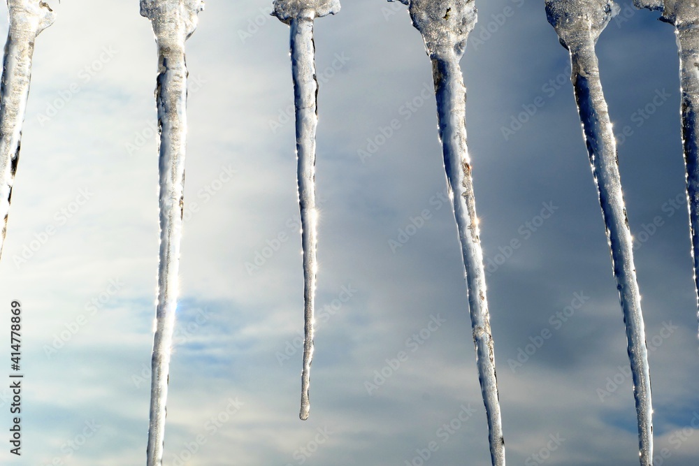 A row of icicles hang side by side, glittering, in the background the winter sky A row of icicles hang side by side, glittering, in the background the winter sky