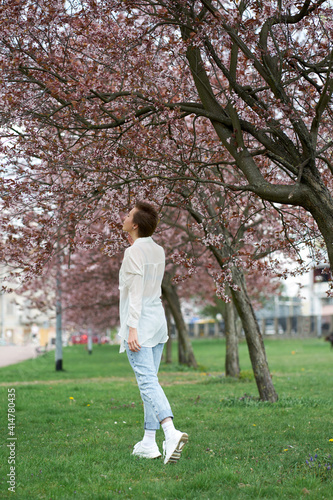 Young pretty redhead woman wearing white stylish blouse and jeans smelling blossoming sakura.
