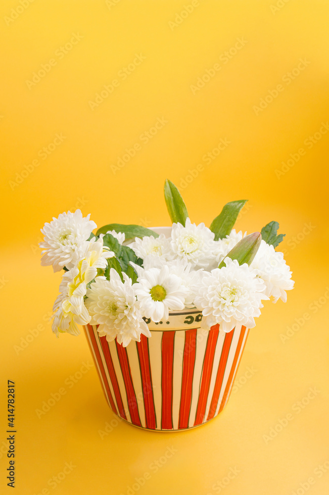 On a yellow background a popcorn bowl full of flowers. Minimalist concept.