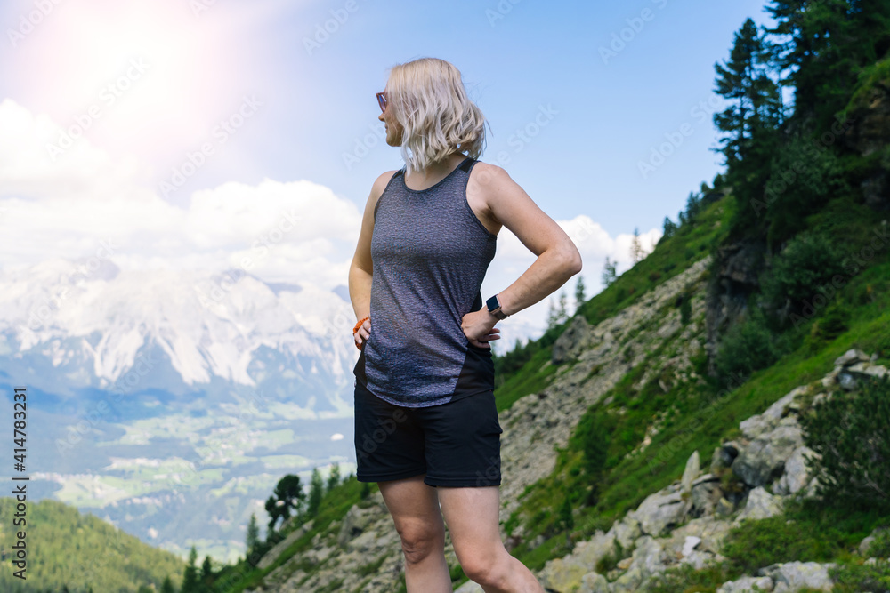 Woman hiking on beautiful summer day in alps mountains Austria, resting on rock and admire amazing view to mountain peaks. Active family vacation leisure with kids. Outdoor fun and healthy activity