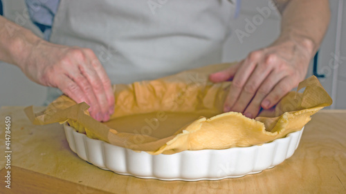 The process of making a base for a shortcrust quiche pie, male hands transfer a rolled dough sheet into a baking dish. Authentic home hobby home baker. Pie crust recipe