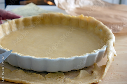 The process of making a base for a shortcrust quiche pie, male hands transfer a rolled dough sheet into a baking dish. Authentic home hobby home baker. Pie crust recipe