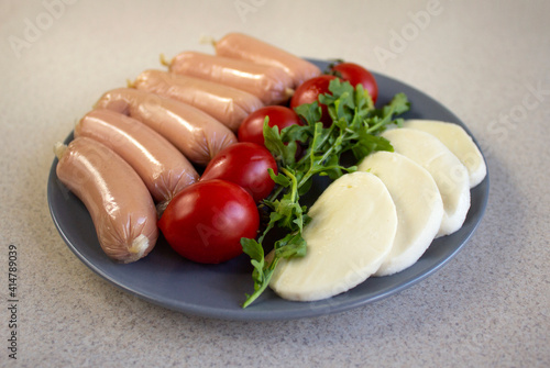 Appetizing sausages and mocarella on grey plate on a marble background, close up photo