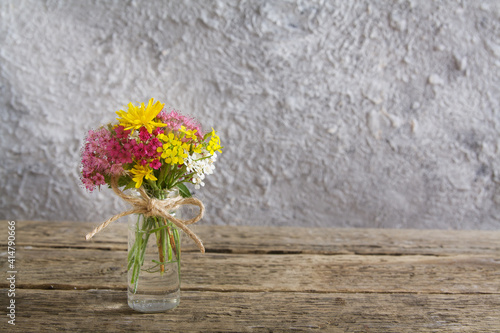 Miniature glass bottle with flowers on wooden table and concrete background with sunlight with copy space