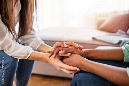 Different ethnicity female friends hold hands during confidential talk close up. Counsellor psychologist provide mental aid to patient at session in clinic, addicted patient professional help concept photo