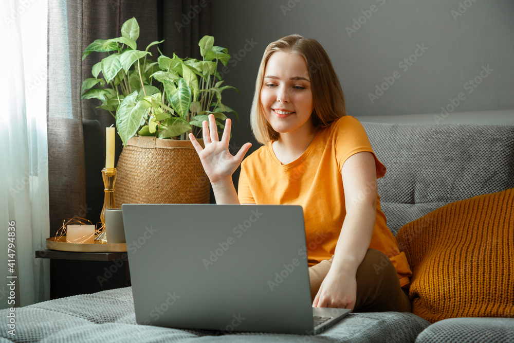 Happy young beautiful woman talking by video call using laptop while sitting on sofa in living room. Remote work study, communication with family and friends in home interior Happy young beautiful woman talking by video call using laptop while sitting on sofa in living room. Remote work study, communication with family and friends in home interior