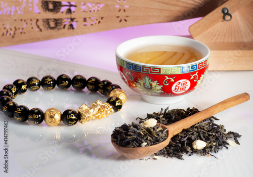 tea in a spoon and teacup with a Chinese fan on the background