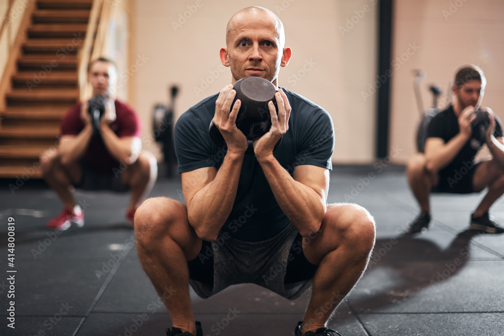 Obraz premium Fit man doing squats with weights during a gym class