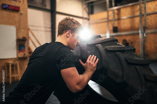 Fit young man doing tire flips in a gym