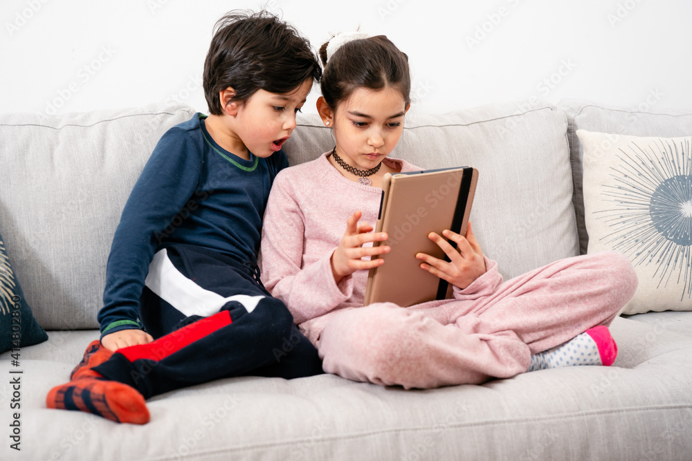 Two mixed-race kids sitting on sofa with tablet. Real life, diversity, digintal technology Two mixed-race kids sitting on sofa with tablet. Real life, diversity, digintal technology