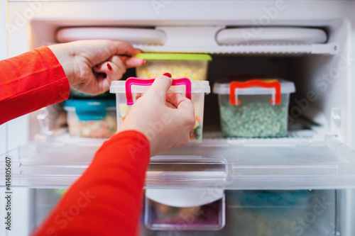 Woman placing containers with frozen vegetables in freezer.