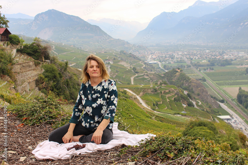 Naklejka premium Woman sitting on the white cloth on the ground where there are some fresh ripe grapes, background has spectacular view of Mountains.Wine production region. Green landscape.