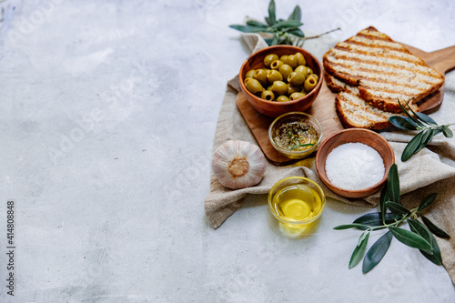 Mediterranean olives with herbs and bread slices on rustic table, top view