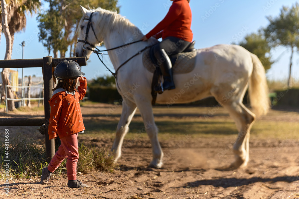 4-year-old girl on horseback greeting her mother who is riding a horse 4-year-old girl on horseback greeting her mother who is riding a horse