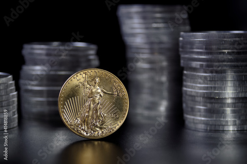 1 ounce gold coin infront of stacks of silver coins