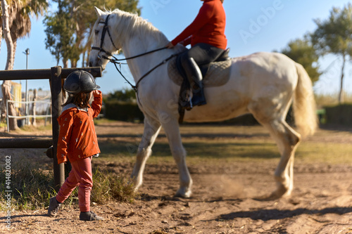 4-year-old girl on horseback greeting her mother who is riding a horse. environment mixed between rural and urban