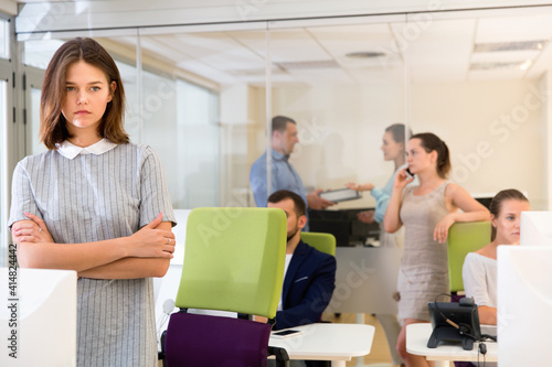 Portrait of young unhappy angry business woman in coworking space with working colleagues behind