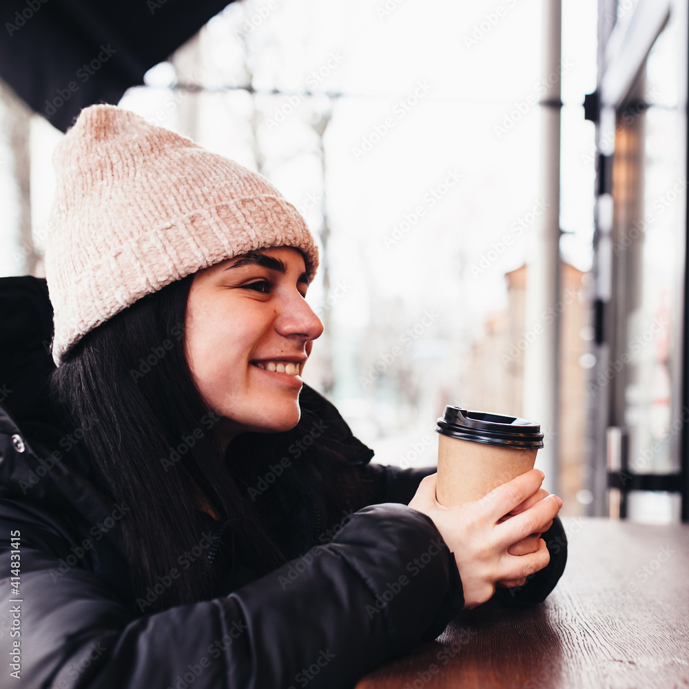 Girl smiling, holds paper cup of coffee in hand near cafe. Blurred background Girl smiling, holds paper cup of coffee in hand near cafe. Blurred background
